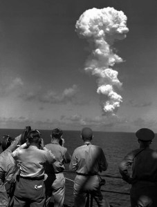 Americans scientists, journalists, and soldiers, watch the explosions from far away.